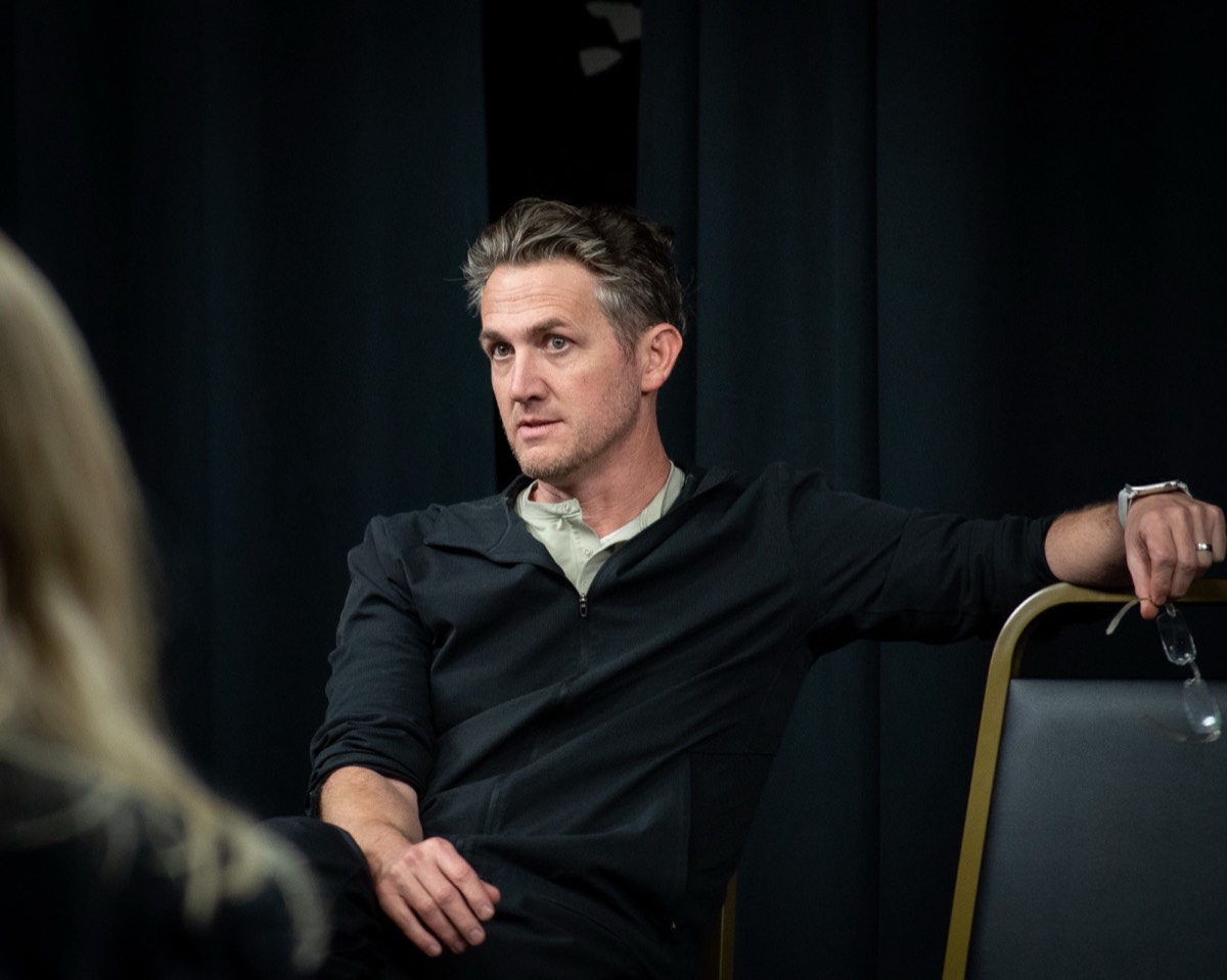Matthew Dearing seated in a black jacket, listening across the room.